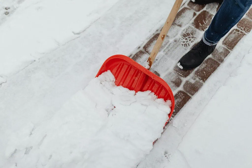 Rote Schneeschaufel räumt Gehweg frei.